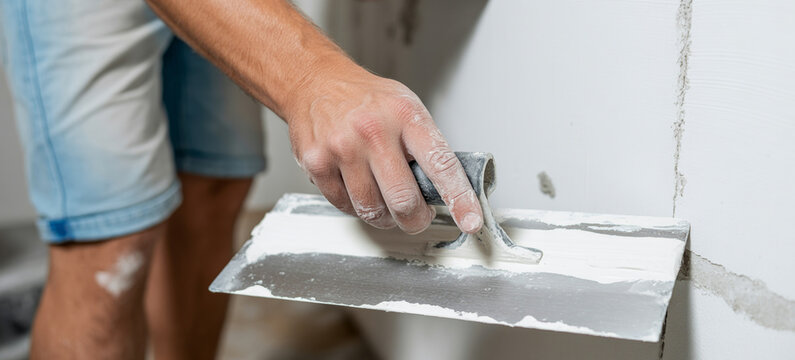 Construction worker plastering a wall with a trowel for home renovation and interior repair