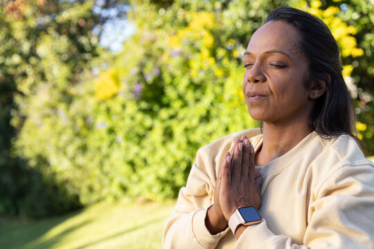 African American woman praying hands pressing eyes closing in yard tan top watch studs, copy space