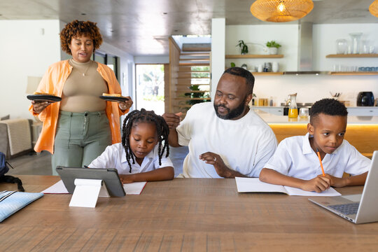 African American family guiding children learning in kitchen with tablet laptop woman in orange top
