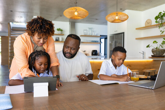 African American family helping daughter on tablet stand while kids in white shirts writing at PC