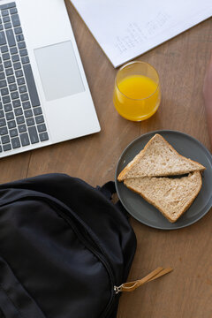Grey plate is holding two whole wheat slices on wooden table near laptop, notebook, orange juice