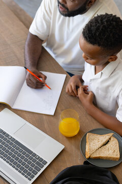 African American father and teen son working at wooden table writing in notebook with orange pencil