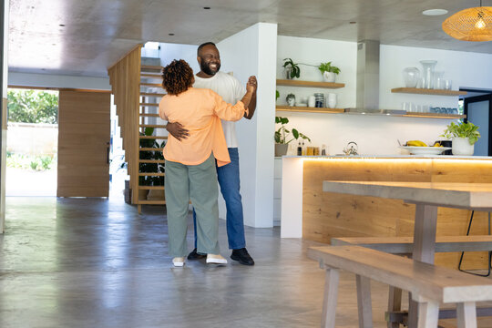 African American couple dancing in modern open-plan kitchen near backlit island with fruit bowl