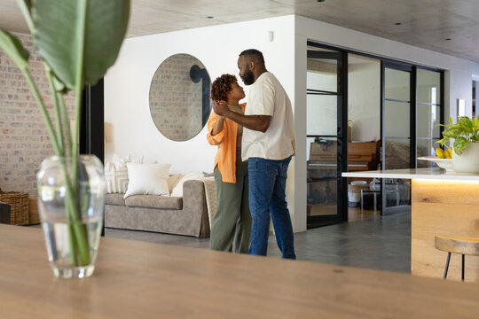 African American couple dancing slowly in open-plan home near beige sofa wearing orange cardigan