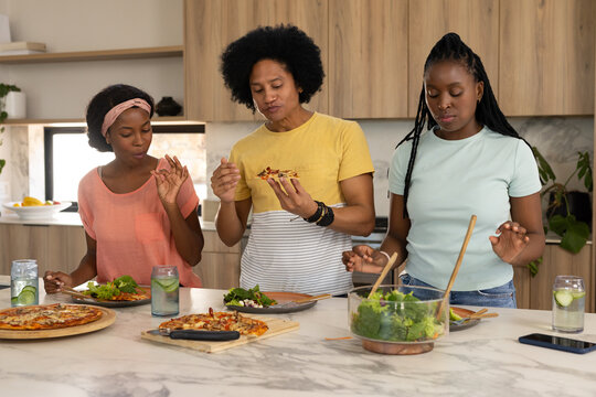 African American family tasting pizza on boards and tossing salad at marble island, wearing apron