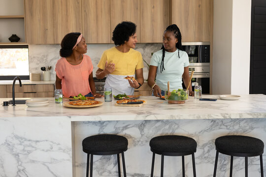 African American women chatting, preparing pizza and serving salad at marble island with smartphone
