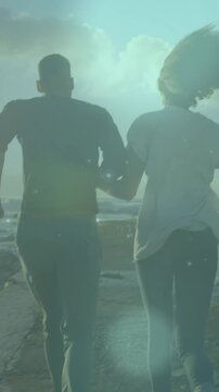 Animation of spots of light over african american couple running on the rocks near the sea