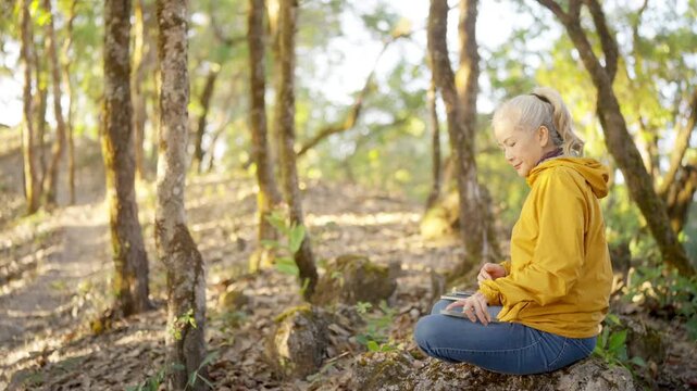 Asian mature woman traveler writing travel journal in notebook while hiking in forest, enjoy relaxation nature therapy, outdoor active lifestyle with mindfulness, mental wellness and self reflection.