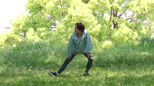 芝生の上で片脚を伸ばして伸脚ストレッチをする女性