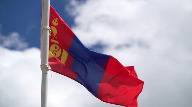 Mongolian flag waving on flagpole against cloudy sky, patriotic national symbol outdoors.
