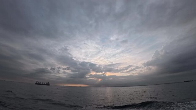 Cinematic real-time wide angle video of dramatic cloudy sky and crepuscular rays over ocean with cargo ship