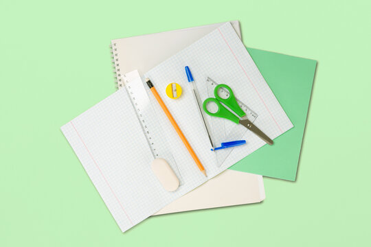 School stationery as checkered notebook, scissor, pencil with eraser, pen with cap, ruler, eraser and pencil sharpener. On green paper surface background. File with Clipping Path.