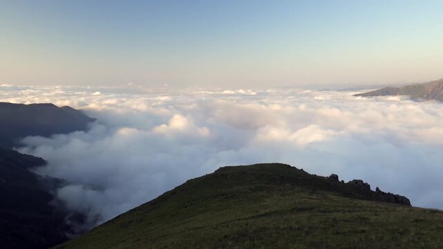 Rize mountain meadow ridge glows at sunrise above clouds with rocky highland terrain.