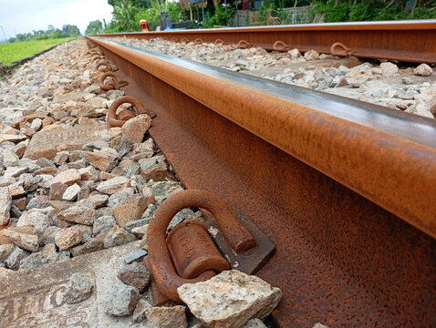 Detailed close-up shot of heavy metal railway rail and fastening clips on rock ballast with steel rail