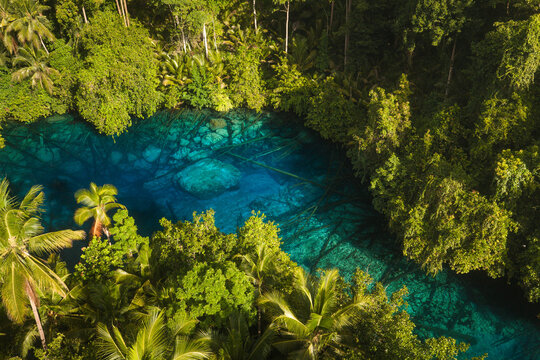 Aerial view of Danau Paisu Pok Luk Panenteng with crystal clear blue water surrounded by lush tropical rainforest and palm trees in Bulagi Utara, Central Sulawesi, Indonesia.
