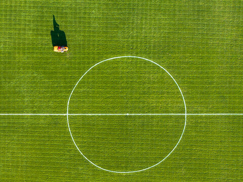 Aerial view of a person operating a lawnmower on a green football field with white markings in Novi Sad, Vojvodina, Serbia.