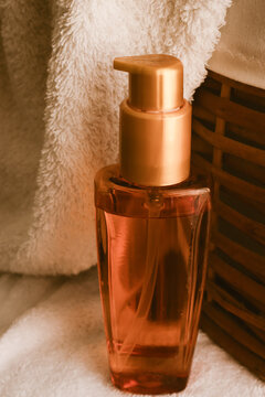 Golden skincare product in a pump bottle standing next to a soft white towel and a wicker basket, illustrating concepts of luxurious spa wellness and daily self-care rituals