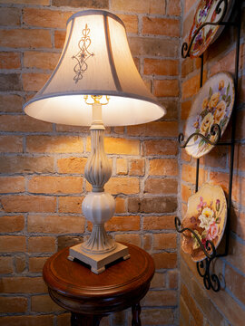 An illuminated antique lamp on a wood table next to a brick wall