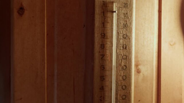 Static close up view of traditional wooden thermometer mounted on wood panel wall showing hot indoor climate inside rustic sauna room during relaxation session.