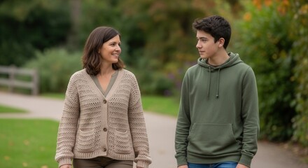 Fototapeta premium Mother and teenage son walking together outdoors, smiling and looking at each other, enjoying a pleasant moment in a park during autumn.