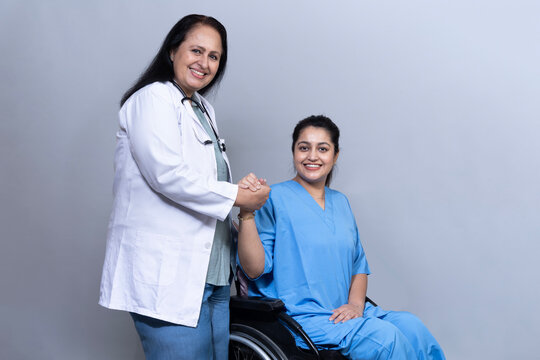 Young Indian woman with a disability sitting in a wheelchair while a female doctor gently holds her hands, representing compassionate medical care, emotional support and inclusive healthcare.