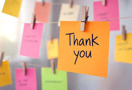 Bright orange sticky note with thank you message hanging among colorful notes and clips