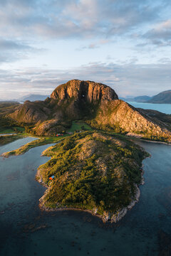 Aerial view of the iconic Torghatten mountain with its natural tunnel, surrounded by lush green coastal landscape and calm blue waters in Bronnoy Municipality, Nordland, Norway.
