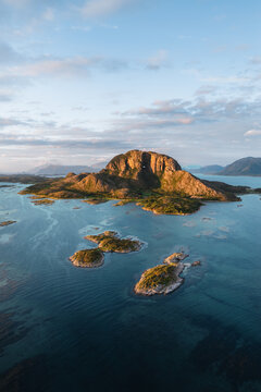 Aerial view of Torghatten mountain with its iconic natural tunnel, surrounded by the blue waters of the Norwegian Sea and scattered islands in Bronnoy Municipality, Nordland, Norway.