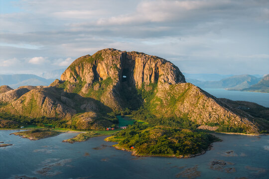 Aerial view of Torghatten mountain with its iconic natural tunnel, surrounded by coastal waters and lush greenery in Bronnoy Municipality, Nordland, Norway.