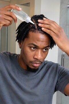 Young black man applying micellar scalp cleanser to his twists looking in the bathroom mirror