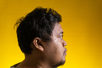 Striking side profile portrait of a young Asian male looking forward against a bright yellow background. The calm individual faces entirely to the right, presenting clear facial contours, © M. Faisal Riza