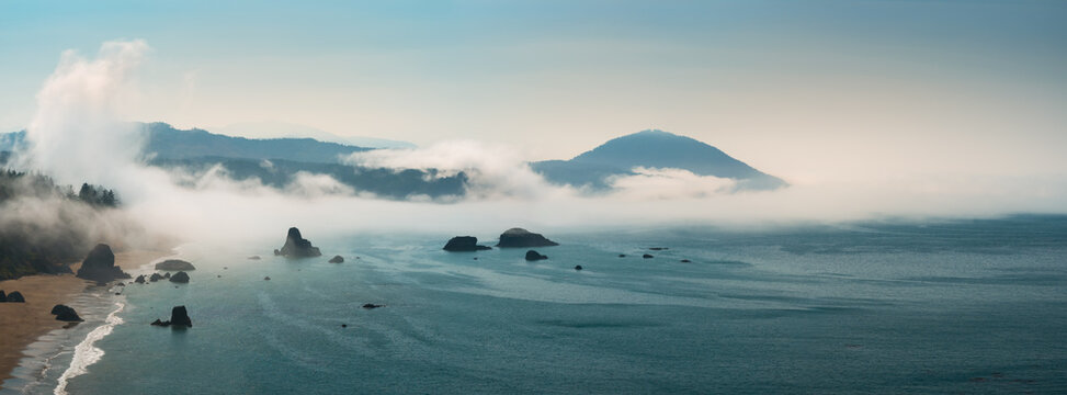 Aerial view of the panoramic Port Orford coastline, with sea stacks rising from the Pacific Ocean, coastal fog, and Humbug Mountain beyond.