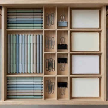 Neatly organized stationery drawer seen from above with dividers holding pens, clips and blank cards