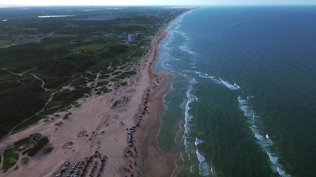 Playa Miramar beach with turquoise Gulf waters, sandy shoreline, coastal vegetation, beachgoers, vehicles and palapas extending toward the horizon, creating a peaceful tropical landscape