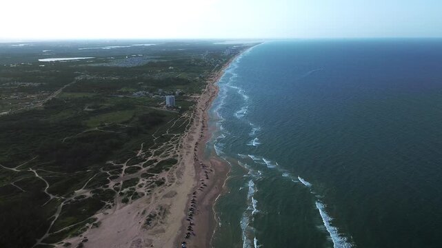 Playa Miramar beach with turquoise Gulf waters, sandy shoreline, coastal vegetation, beachgoers, vehicles and palapas extending toward the horizon, creating a peaceful tropical landscape