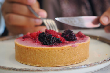 A person cuts a berry tart while sitting in a cafe during the afternoon., © Towfiqu Barbhuiya 