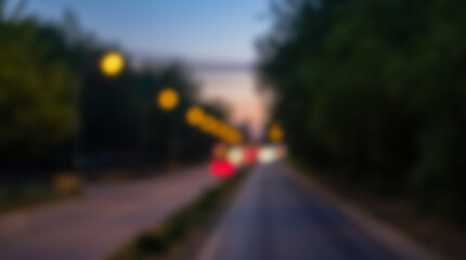 Fototapeta premium Blurry road at dusk with car lights and trees.