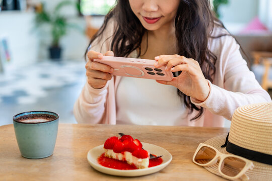 Phone eats first and food photography concept: Woman photographing delicious strawberry dessert with her smartphone before eating
