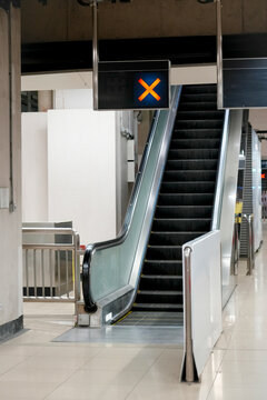 Stationary escalator stands quiet in a sterile transit terminal with a bright glowing warning symbol blocking entry for commuters during the early morning hours