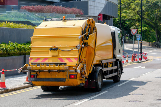 Sanitation vehicle driving on a paved street near modern architecture as it performs essential cleanup services within the bustling metropolitan landscape