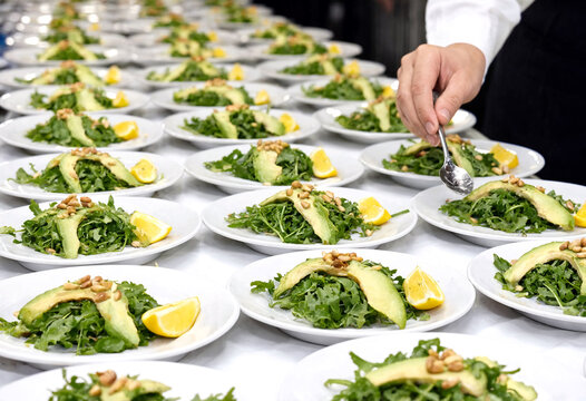 Closeup of freshly prepared avocado and arugula salad plates being garnished by chef