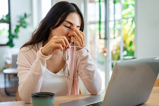 Eye strain, vision health, and fatigue concept: Stressed woman taking off glasses to rest her eyes during laptop work.
