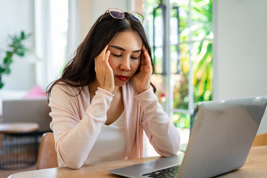 Tired Asian woman sitting at desk, feeling dizzy and exhausted from heavy laptop workload