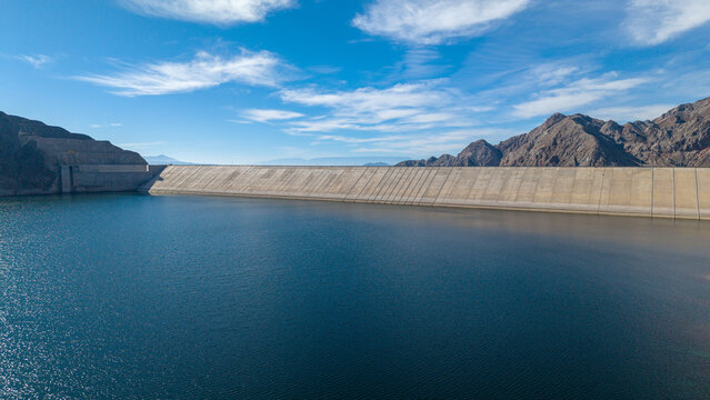 Aerial view of Dique Punta Negra dam with its concrete wall holding back reservoir water, surrounded by arid mountains under a clear sky in Zonda Department, San Juan Province, Argentina.