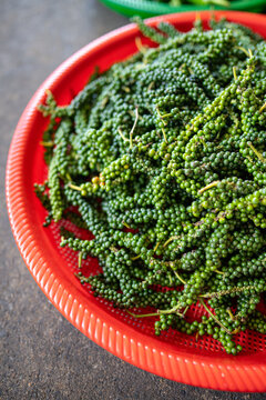 Plastic basket filled with pile of fresh green peppercorns on stem, unripe Piper nigrum vine berries, street food market selling mild green peppercorns, culinary spice highly prized in Southeast Asia.