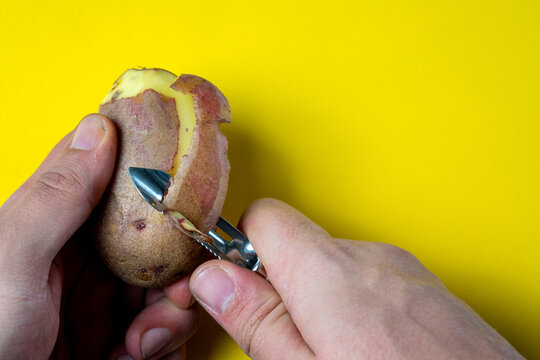 Hands peeling a potato with a vegetable peeler