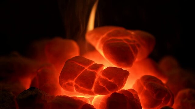 Glowing charcoal briquettes with smoldering embers and faint rising smoke against dark background, showing intense heat, cracked porous texture, and dramatic red orange light