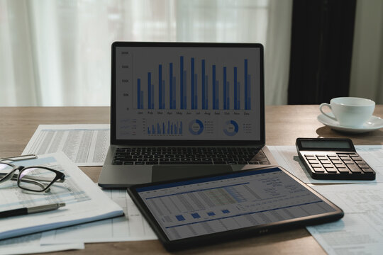 Laptop and tablet display charts and spreadsheets beside calculator and printed financial documents, presenting market analysis, data comparison, budgeting, and business reporting workflow.