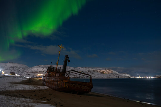 View of an old fishing ship on a sandy beach under the northern lights