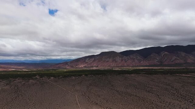 Mountain landscape near Recta del Tin Tin Highway with desert plain under dramatic clouds, aerial panoramic orbit, Salta Region Argentina